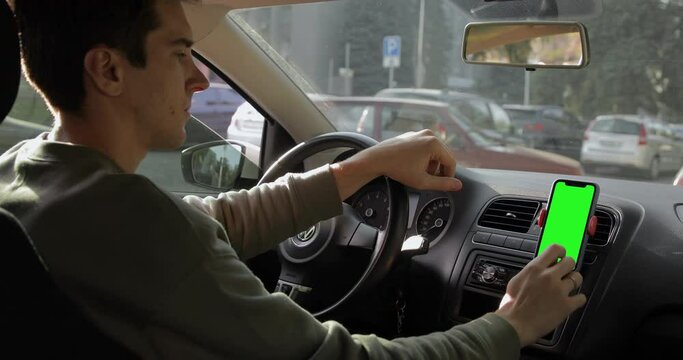 Man driver staying in the parking lot and using smartphone navigator maps on iPhone. Pre-keyed green screen ready to be replaced with your content. Autumn season. 