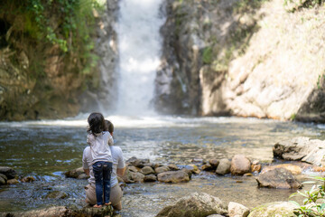 Mother and daughter sitting at the rocks against waterfall in woods forest.