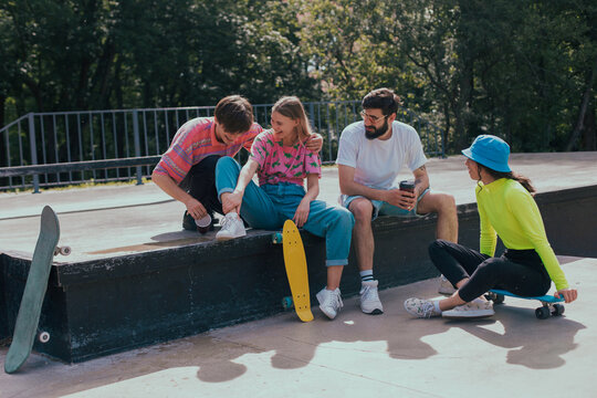In a good sunny day, group of friends very attractive multiethnic enjoying the time in a modern, skate park they sitting on the floor and socializing before start to skateboarding