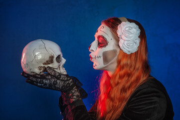 Beautiful woman with scary Halloween make up dead day calavera style kissing human skull