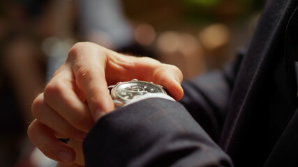 Unrecognizable man looking at wrist watch in park. Guy hiding watch under sleeve
