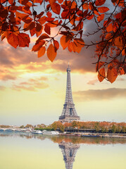 Eiffel Tower with autumn leaves against colorful sunset in Paris, France