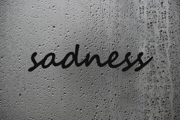Inscription a sadness written on wet window after rain