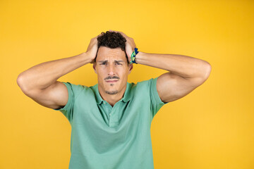 Young handsome man wearing green casual t-shirt over isolated yellow background suffering from...