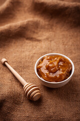 Altai meadow honey in a white bowl near a wooden Mace for honey on burlap close-up.