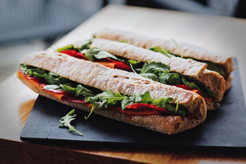 Healthy fresh crusty baguette submarine sandwich with salami, cheese and rucola. Selective focus