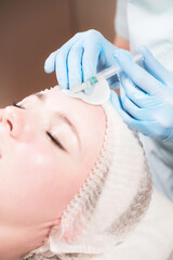 Woman professional beautician conducts an injection of botox or hyaluronic acid to a client in a beauty salon