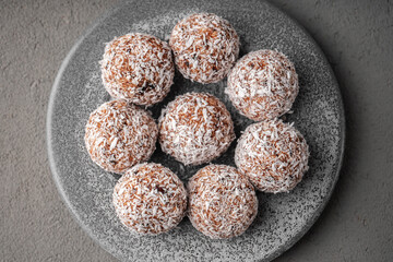 Round vegetarian sweets made of dates and coconut shavings lie on a grey concrete plate on a grey concrete table top view