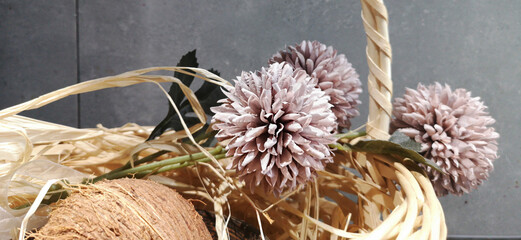 A wooden basket with soft pink fake flowers and a coconut.
