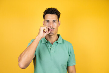 Young handsome man wearing green casual t-shirt over isolated yellow background mouth and lips shut...