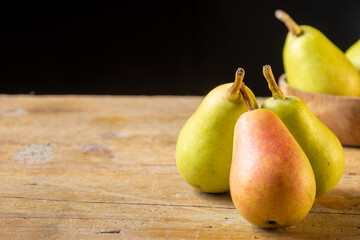 Top view of ercolinas pears grouped on wooden table and black background horizontally with copy space