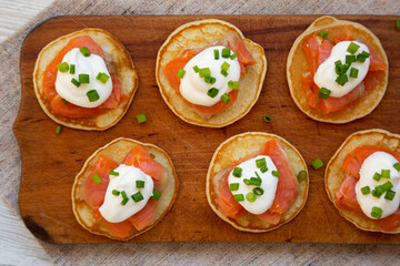Homemade Blini with Smoked Salmon, Creme and Chives on a rustic wooden board, top view. Flat lay, overhead, from above.