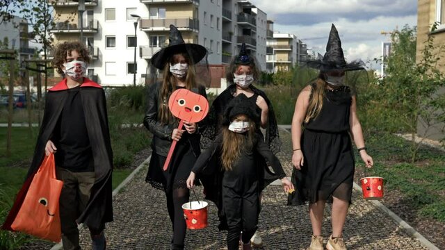 Group of children in black masquerade costumes are walking down the street. Everyone has medical masks on their faces. Halloween during the covid19 coronavirus pandemic.