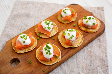 Homemade Blini with Smoked Salmon, Creme and Chives on a rustic wooden board, side view.