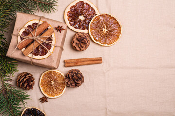 Christmas composition with handmade kraft paper gift box, dried citrus slices, cinnamon, anise, pine cones and fir tree branches, top view copy space