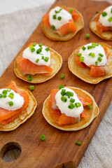 Homemade Blini with Smoked Salmon, Creme and Chives on a rustic wooden board, low angle view.