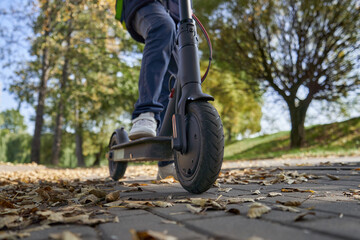 Obraz premium The boy is riding on the electric scooter through the park