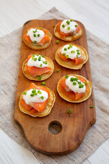 Homemade Blini with Smoked Salmon, Creme and Chives on a rustic wooden board, low angle view.