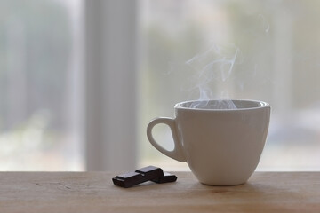 A cup with a hot invigorating drink of coffee or tea in front of a window bathed in the morning sun. A cozy photo with a blurred background