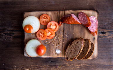 Sausage slices on a wooden Board,with slices of tomatoes,onions with slices of bread,still life