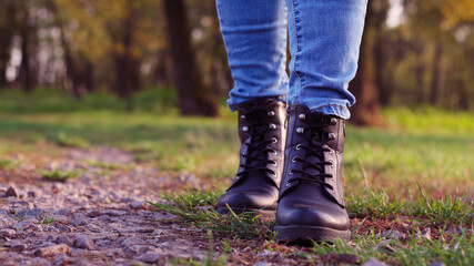 Close-up of female legs in lace-up shoes and jeans are walking along a forest road. Healthy lifestyle, walking in the fresh air in the park.