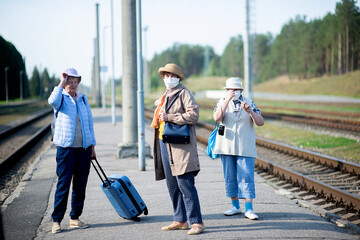three old senior elderly women on the platform waiting for train and wearing a face mask