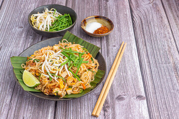 Pad Thai served with vegetables and lemon slice on banana leaves in black dish on wooden table. Thai food famous. Top view with copy space. Concept of Thai traditional foods
