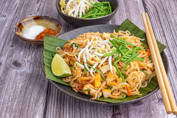 Pad Thai served with vegetables and lemon slice on banana leaves in black dish on wooden table. Thai food famous. Top view with copy space. Concept of Thai traditional foods