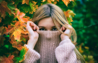 Beautiful girl wrapped in a knitted sweater in the autumn Park.