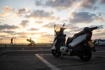 Motorbike on a parking lot, jogger and surfer in front of the sea at sunset