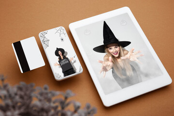Young woman in black hat on device screen and brown background. Attractive caucasian female model. Halloween, black friday, cyber monday, sales, party, autumn concept. Tablet and money card.