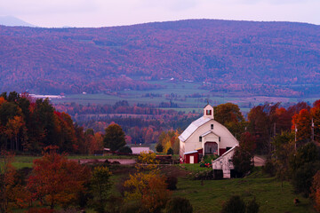 vintage white barn in the valley of vibrant hills and mountains during fall changing colors in new hampshire USA 