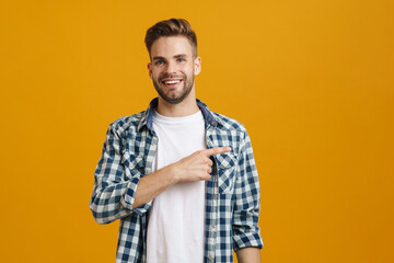Joyful handsome unshaven guy smiling and pointing finger aside