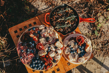 Front view of the table with meat plateau with fruits and berries snacks , frying pan with mushrooms.