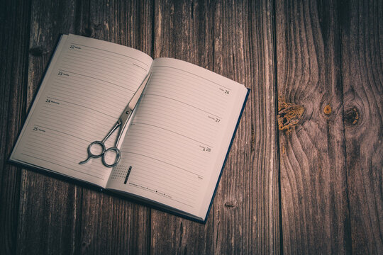A pair of hairdressing scissors laid on an open diary laid on a rustic wooden table