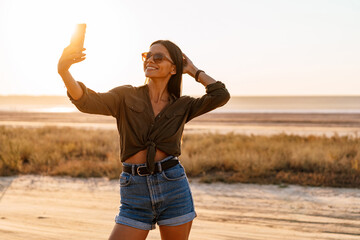 Beautiful joyful girl taking selfie on cellphone on nature