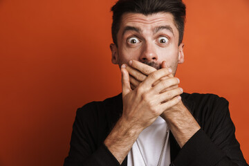 Photo of young shocked man covering his mouth with hands