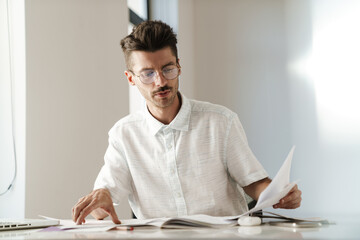 Photo of serious unshaven man working with laptop and papers at table