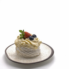 Meringue topped with whipped cream. Top decorated with fresh strawberries, blueberries. The saucer is beige with brown dots and a border. Isolated on white background. Lower left corner. Copy space.