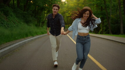 Fototapeta premium Energetic couple moving fast on road in park. Man and woman having fun outdoors