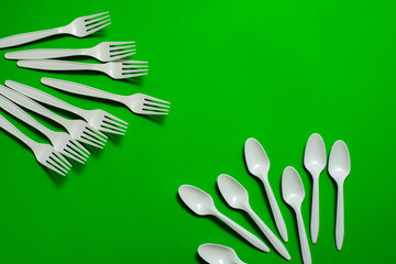 many organic cornstarch forks and spoons on green background. biodegradable tableware. eco...