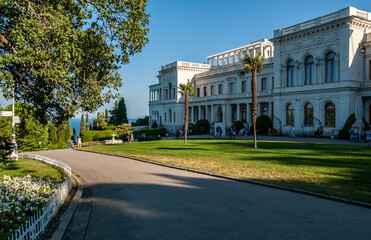 The palace in the Italian style, a green area with palm trees, a group of tourists, you can see the sea, blue sky. Crimea, Livadia Palace in early 20th century.