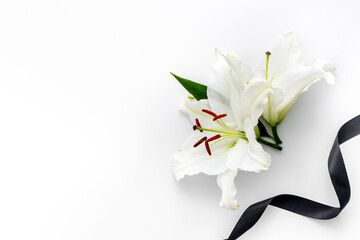 Flat lay of lily flowers and black ribbon. Funeral symbol