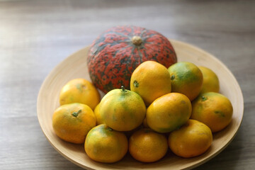 Bowl with tangeriens and pumpkin on wooden table. Selective focus.