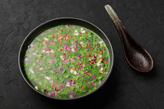 Pachi Pulusu in black bowl on dark slate table top. Raw Tamarind Rasam is indian cuisine soup dish. Asian food and meal.