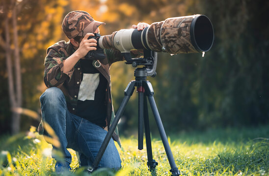 wildlife photographer using telephoto lens with camouflage coating photographing wild life using gimbal head on tripod. professional photography equipment for cinematic shooting in the nature outdoor - Powered by Adobe