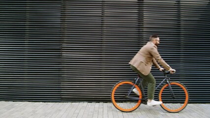 Side view medium shot of Caucasian businessman in smart casual outfit riding bicycle along urban wall on city street while going to office in the morning - Powered by Adobe