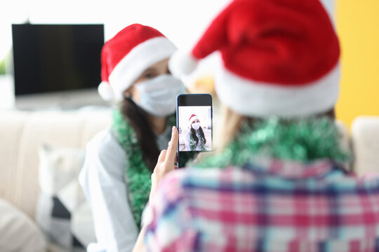Woman photograph her friend on phone in santa claus hat and tinsel. Pastime with family for new year and christmas.