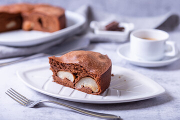 Piece of chocolate pie with pear. In the background is a pie, a cup of coffee and pieces of chocolate. Close-up.
