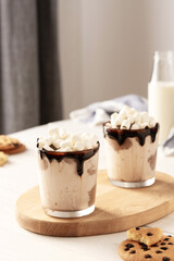 Milkshake with ice cream, marshmallows and chocolate, a glass with a milkshake on a wooden board, chocolate chip cookies and a bottle of milk